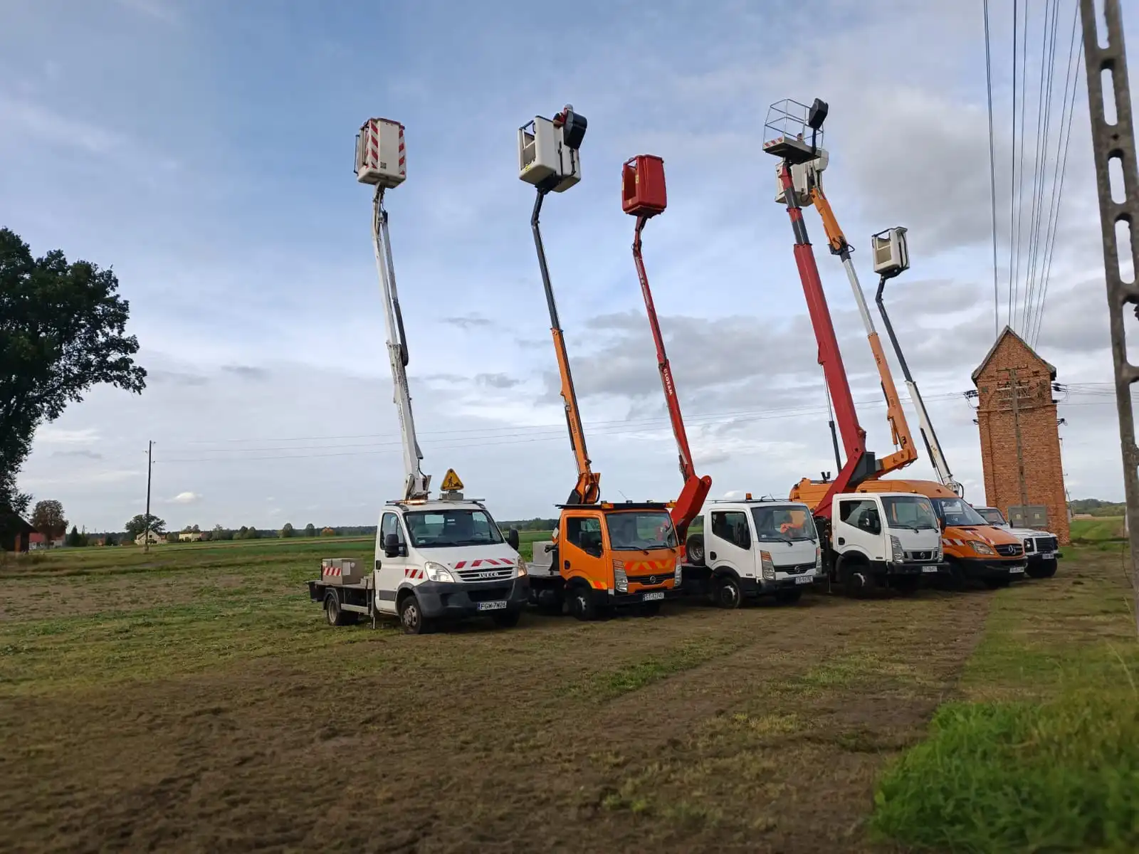 Zdjęcie przedstawiające samochody naszej floty z rozłożonymi podnośniki koszowe, którymi świadczymy usługi ścinania drzew oraz przycinania gałęzi